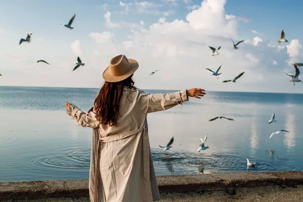 Young happy asian woman with hands in the air walks on the seaside in autumn. Seagulls flying on the beach.