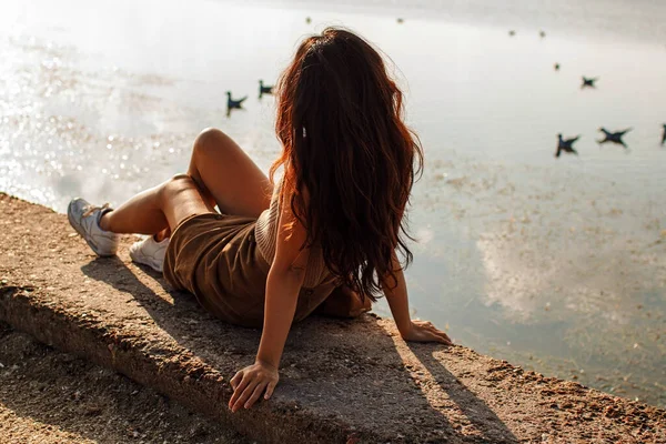 Düşünceli bir kadın kumlu sahilde oturmuş, bulutlu bir göle ve uçan martılara bakıyor.. 