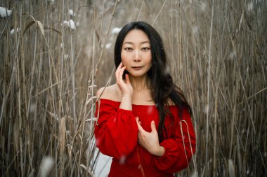 Young beautiful asian woman in long red dress near the reeds over winter background. Fairy tale girl on winter landscape.