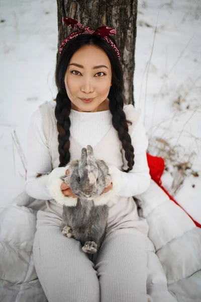 亚洲女孩抱着一只兔子在雪地的森林里 与复活节兔子的友谊 — 图库照片