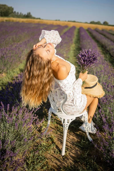夏にラベンダー畑で屋外でリラックスしながら花の花束を身に着けている白人の若い女性の写真 — ストック写真