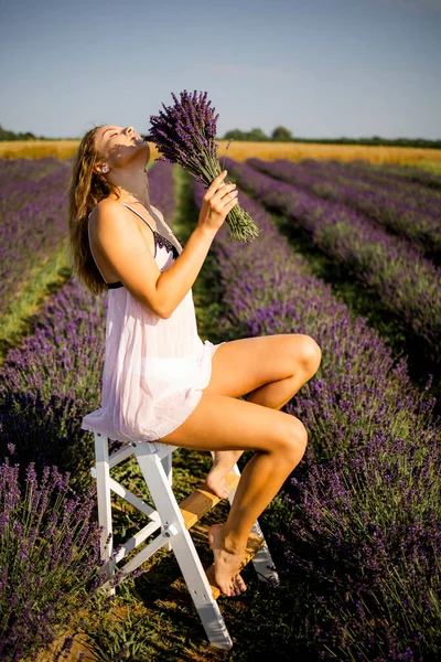 夏にラベンダー畑で屋外でリラックスしながら花の花束を身に着けている白人の若い女性の写真 — ストック写真