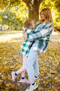 Sonbahar parkında kızıyla birlikte oynayan neşeli bir kadının portresi..