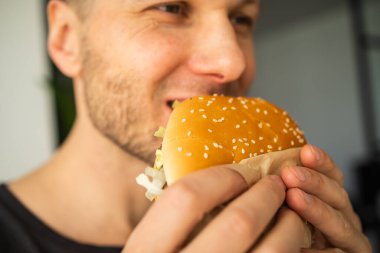 Genç adam taze, lezzetli bir hamburgeri ısırıyor.
