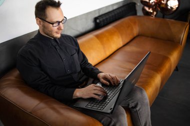 Gülümseyen iş adamı ofisin lobisinde oturuyor ve bir dizüstü bilgisayar üzerinde çalışıyor. Ofis lobisinde çalışan bir erkek işadamı..