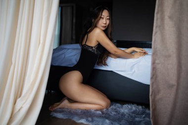 Mükemmel bronz tenli, seksi Asyalı kadın. Sana poz veriyor. Çekici siyah iç çamaşırı giyiyor.. 