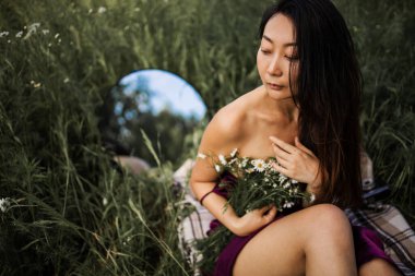 Papatya tarlasında ayna ile oturan güzel Asyalı genç bir kadın. Uzayı kopyala Meditasyoncu hayalperest. seçici odak