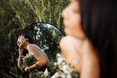 Papatya tarlasında ayna ile oturan güzel Asyalı genç bir kadın. Uzayı kopyala Meditasyoncu hayalperest. seçici odak