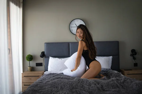 아름다운 여자가 베개를 껴안고 집에서 침대에 뛰어오르는 — 스톡 사진