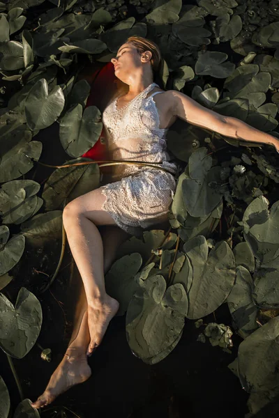 一个漂亮的红头发女孩穿着白色的衣服 在河里摆姿势 放着睡莲 欧菲莉亚的童话 — 图库照片