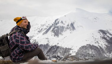 Sırt çantalı aktif turist karlı dağın tepesindeki manzaranın tadını çıkarıyor.