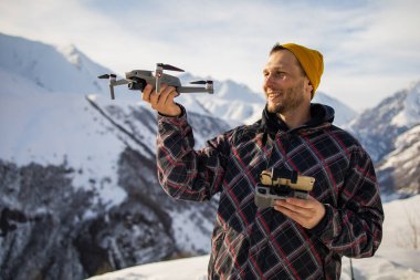 Genç video yapımcısı karlı dağlarda İHA uçuruyor ve ellerinden bir İHA fırlatıyor. İnsansız hava aracından seyahat içeriği oluşturuluyor