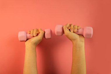 Bir kadının eli pembe arka planda izole edilmiş pembe bir dambılı tutar. Evde eğitim için ekipman. Fitness ve aktivite. Spor ve sağlıklı yaşam tarzı kavramı. 