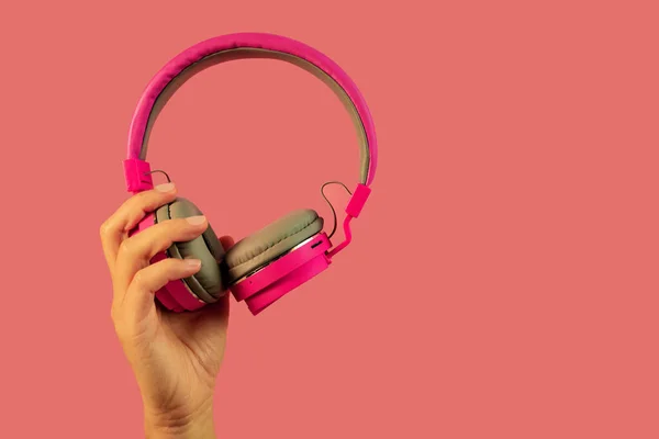 ピンクのヘッドフォンを手に持ってピンクの背景に隔離 — ストック写真
