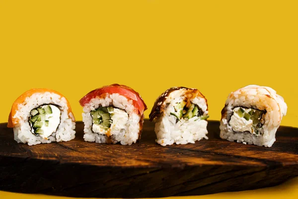 Sarı arka planda somon, avokado, ton balığı ve salatalıklı dört maki rulosu. Pirinç ve nori ile taze hosomaki parçaları. Suşi dürümlü lezzetli Japon yemeklerini yakından çek..