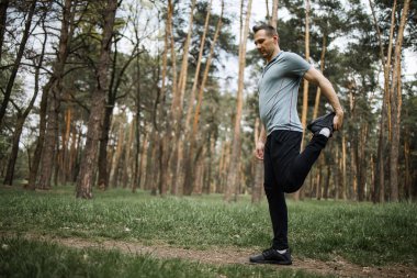 Erkek koşucu esneme egzersizi yapıyor, parkta sabah antrenmanına hazırlanıyor.