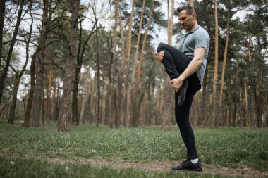 Erkek koşucu esneme egzersizi yapıyor, parkta sabah antrenmanına hazırlanıyor.