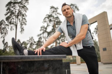 Erkek koşucu esneme egzersizi yapıyor, parkta sabah antrenmanına hazırlanıyor.