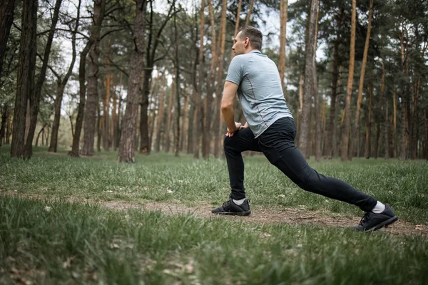 Erkek koşucu esneme egzersizi yapıyor, parkta sabah antrenmanına hazırlanıyor.