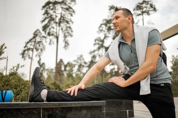 Erkek koşucu esneme egzersizi yapıyor, parkta sabah antrenmanına hazırlanıyor.