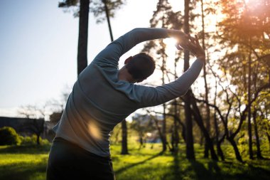 Gün batımında parkta koşan genç bir adam sağlıklı yaşam tarzı egzersizi yapıyor.