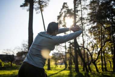 Gün batımında parkta koşan genç bir adam sağlıklı yaşam tarzı egzersizi yapıyor.