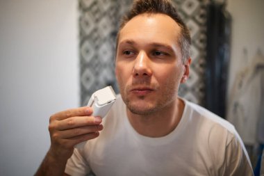 Sakalını budayarak sakalını kesen yakışıklı genç bir adam.