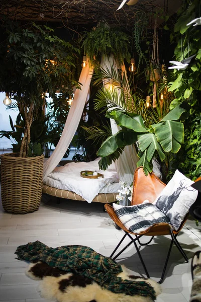 Stylish bedroom interior with green tropical  plants and round bed Bed with baldachin in bohemian style.
