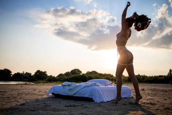 Gün batımında göl kenarında poz veren seksi beyaz dantelli iç çamaşırlı güzel bir kadın..