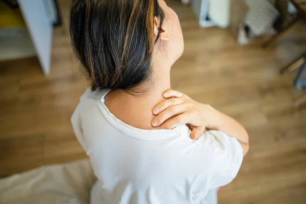 Shoulder pain. Forearm pain, people with body muscle problems, healthcare and medicine concept. Attractive woman is sitting on the bed and holding her sore shoulder with her other hand.