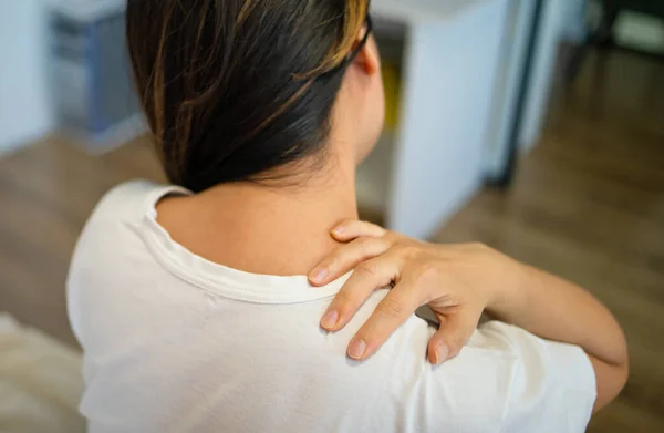 Shoulder pain. Forearm pain, people with body muscle problems, healthcare and medicine concept. Attractive woman is sitting on the bed and holding her sore shoulder with her other hand.