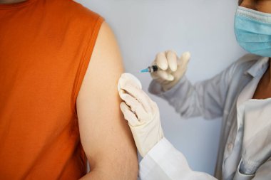 Tıbbi maske takan bir hastaya iğne yapmadan önce elinde şırınga tutan ve pamuk kullanan bir doktorun fotoğrafını çek. COVID-19 veya coronavirüs aşısı