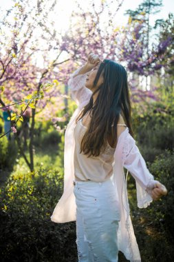 Bahçede tarımsal çiçek arka planında duran muhteşem Asyalı kadın. Bahar çiçekleri..