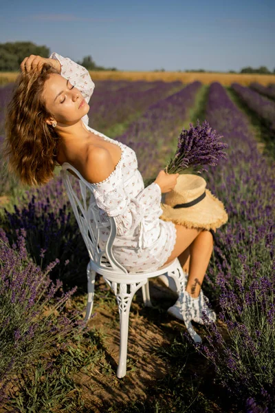 美しい女の子は 素晴らしい開花ラベンダー畑を散策しながら ブーホーシックなドレスとわらの帽子でドレスアップします — ストック写真