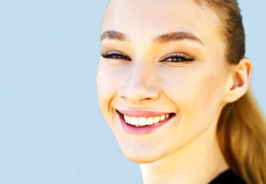 Mükemmel ciltli, doğal makyajlı ve güzel gülümseyen mutlu genç bir kadın. Mavi arka planda beyaz dişli kadın portresi.