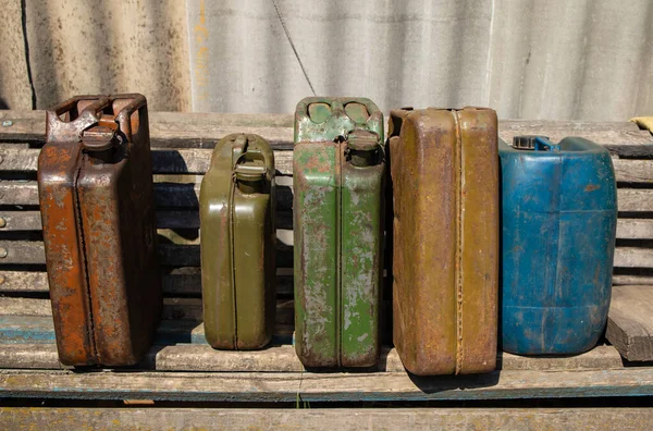 A group of old metal jerry cans with gasoline  stand on shelves in a wooden shed