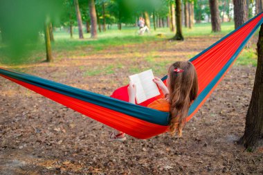 Kitap okuyan gülümseyen bir kadın, ormandaki hamakta dinleniyor, boş zaman ve yaz tatili konsepti