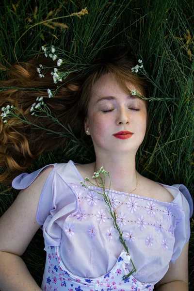 美丽的小女孩 长长的红色卷曲的头发 闭上着眼睛的女孩躺在绿草上 从上往下看 — 图库照片