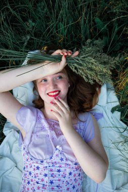 Kızıl saçlı, güzel, genç, kızıl saçlı bir kadının portresi. Bahar güneşinde uzanmış, yeşil çimlerin üzerinde dinleniyor..