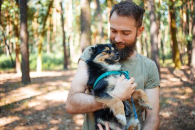 Yakışıklı sakallı adam parkta köpeğini kucaklıyor..
