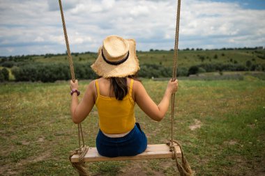 Tanınmayan bir kız, sakin ve güneşli bir günde sallanıyor. Kadın ahşap bir salıncakta oturur ve tarlaya bakar.. 
