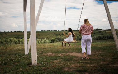 Cheerful lady in white dress leaning back in her swing in sunny golden countryside.