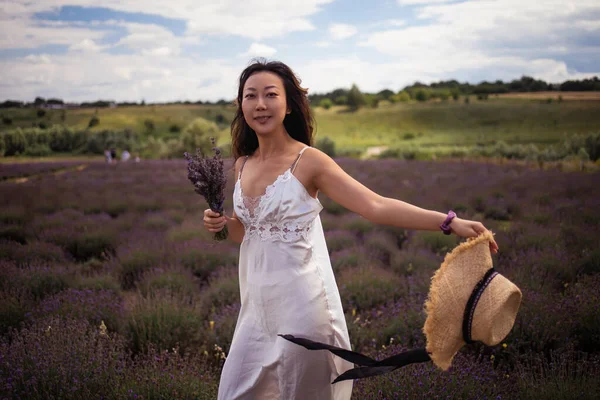 young beautiful elegant asian woman in white dress holding bouquet of lavender flower walking in bloom field outdoors leisure lifestyle