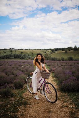 Young asian girl in a white silk dress with a retro bicycle walks on a lavender field.