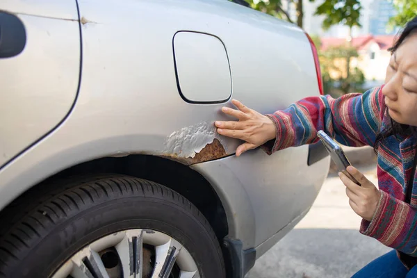 A woman shows rust on a car door from winter reagents. Close-up, selective focus on rust and hand.