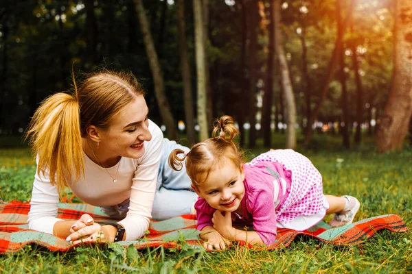 Beautiful young mother with her two years old daughter playing on the grass
