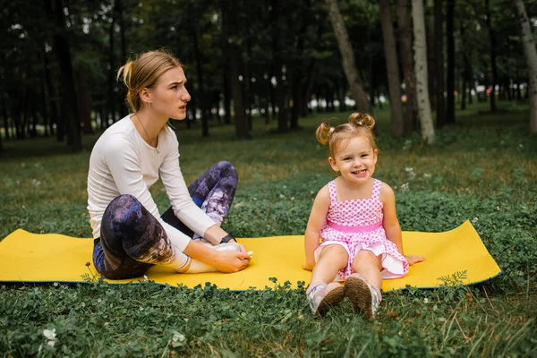 family mother and daughter doing fitness, yoga, exercise on green grass outdoor.