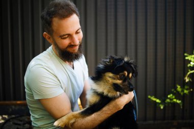 Yakışıklı sakallı adam parkta köpeğini kucaklıyor..