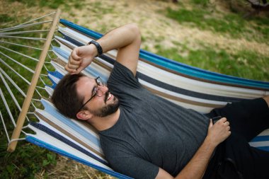 young happy caucasian man swinging in a hammock on a pleasant summer weekend morning in garden. 