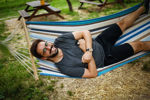 young happy caucasian man swinging in a hammock on a pleasant summer weekend morning in garden. 